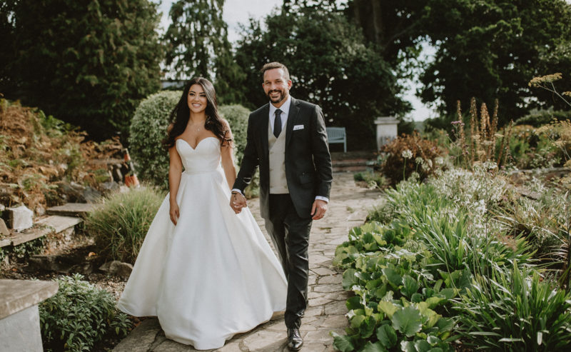 Bromley Court Hotel - A bride and groom walking down a path in a garden during their wedding ceremony.