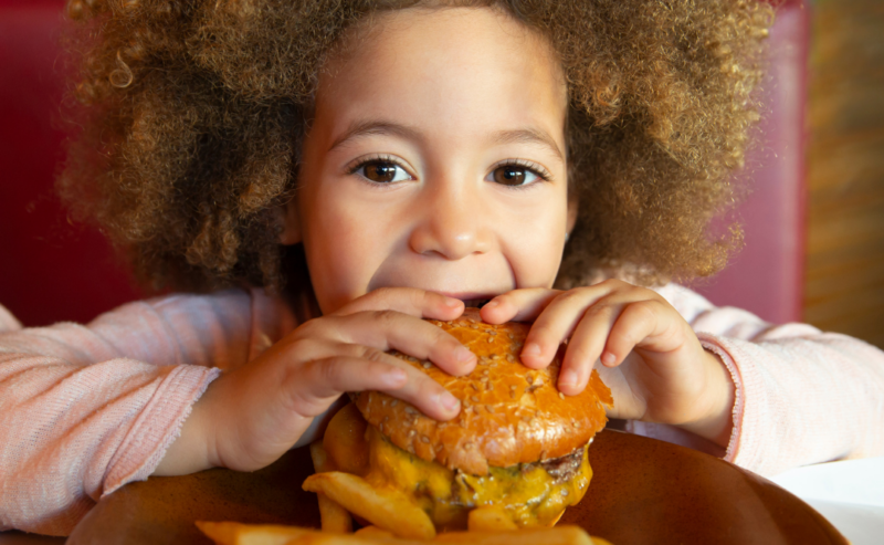 Bromley Court Hotel - A young child with curly hair smiling while holding a hamburger, with a plate of fries in front on the test page.